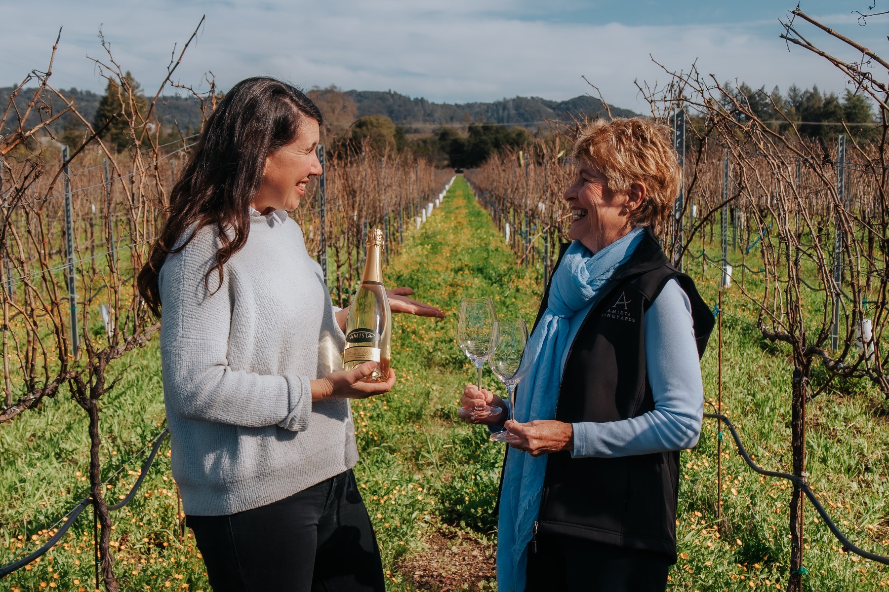 Amista Winemaker Ashley Herzberg and Owner Vicky Farrow in Vineyard with Bottle of Blanc de Blanc